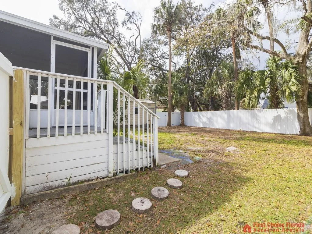 Backyard view featuring a white fenced yard, mature palm trees, and a screened porch with white railings.