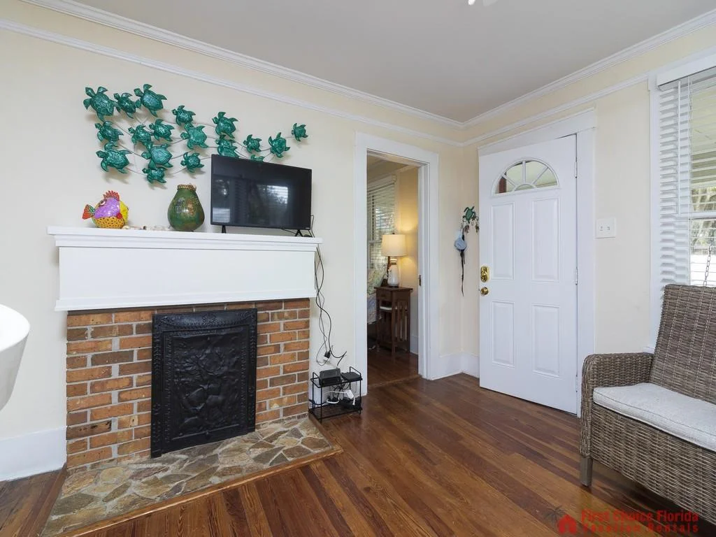Brick fireplace with black cast iron insert is topped by a white mantel holding a TV and decorative pottery.