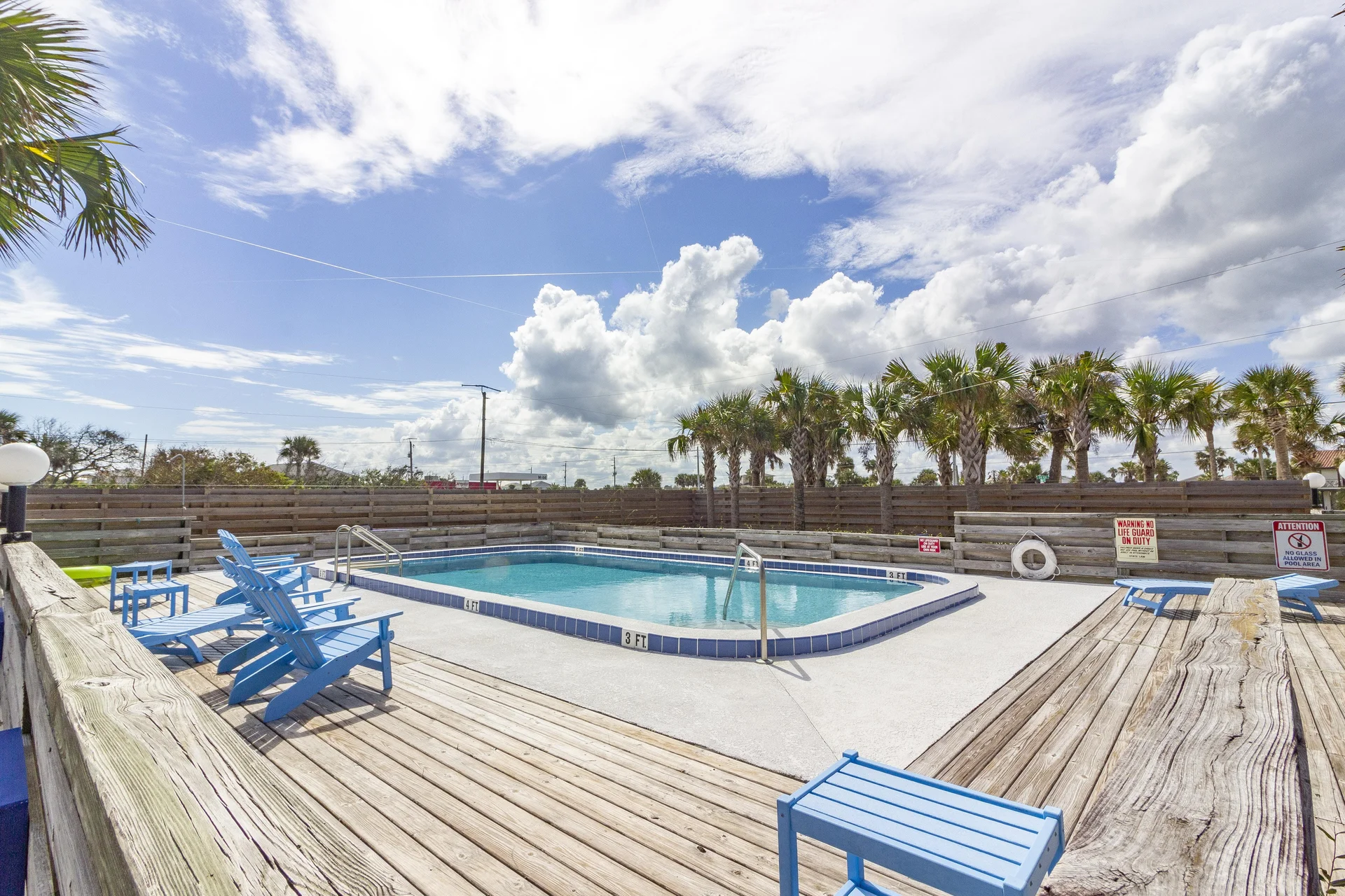 Communal pool with blue tile trim surrounded by weathered wood decking and bright blue Adirondack chairs.