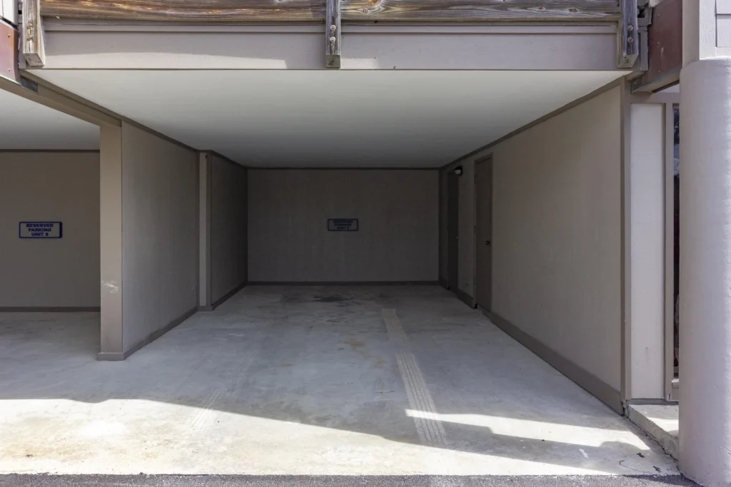 Covered parking space with smooth concrete floor, taupe walls, and adjacent storage doors.