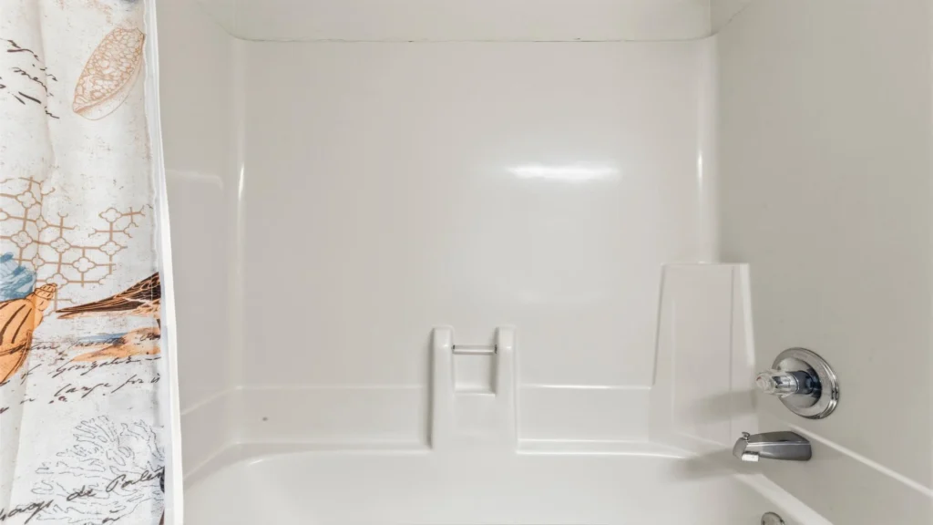 White acrylic bathtub and shower surround with chrome faucet and seashell-patterned shower curtain.
