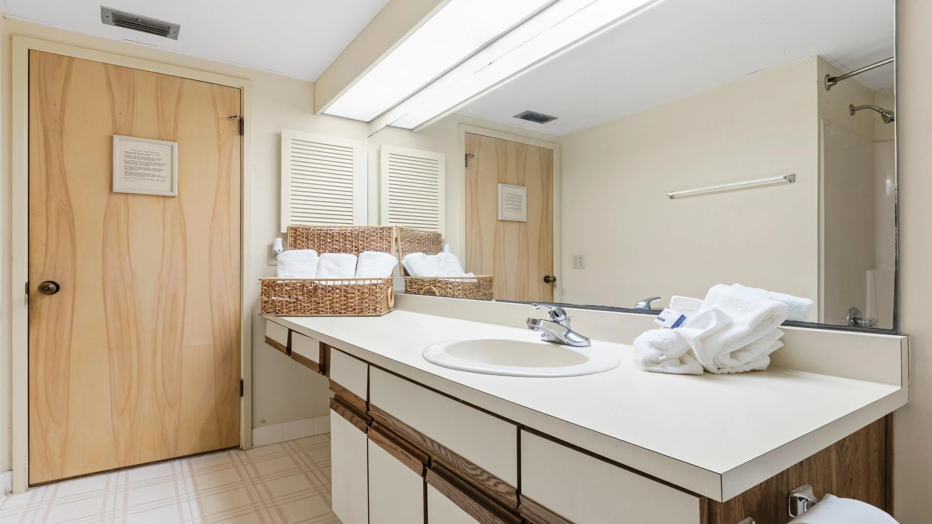 Bathroom sink countertop with built-in basin, wicker basket holding rolled towels, and large mirror above.