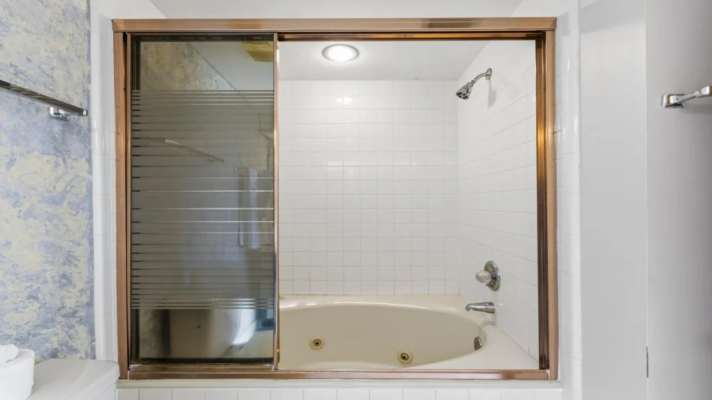 Bathroom features a white tiled tub with sliding glass doors and a built-in showerhead above.