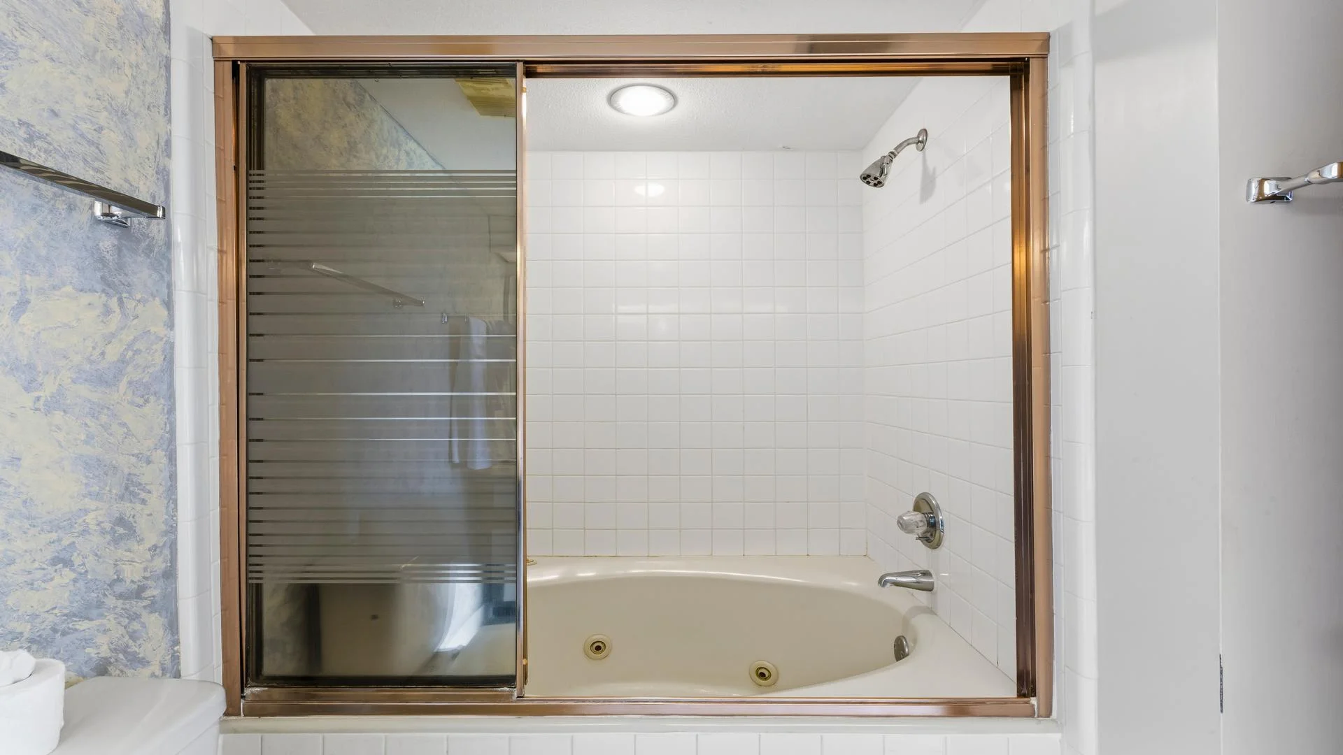 Bathroom features a white tiled tub with sliding glass doors and a built-in showerhead above.