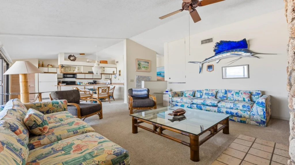Living room features patterned sofas, bamboo armchairs, glass coffee table, and a mounted blue sailfish on cream walls.