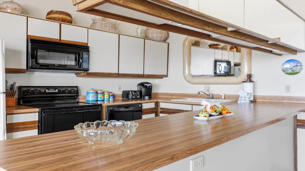 L-shaped kitchen countertop with wood grain finish, black appliances, and overhead cabinets with wicker baskets.