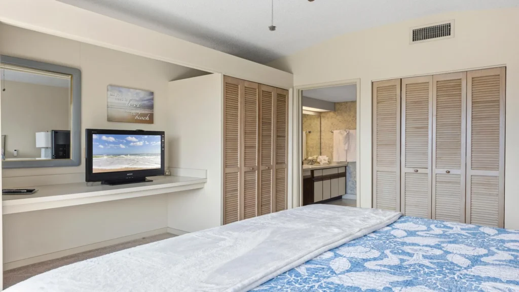 Bedroom view featuring a blue seashell-patterned bedspread, closet with louvered doors, and a wall-mounted TV.