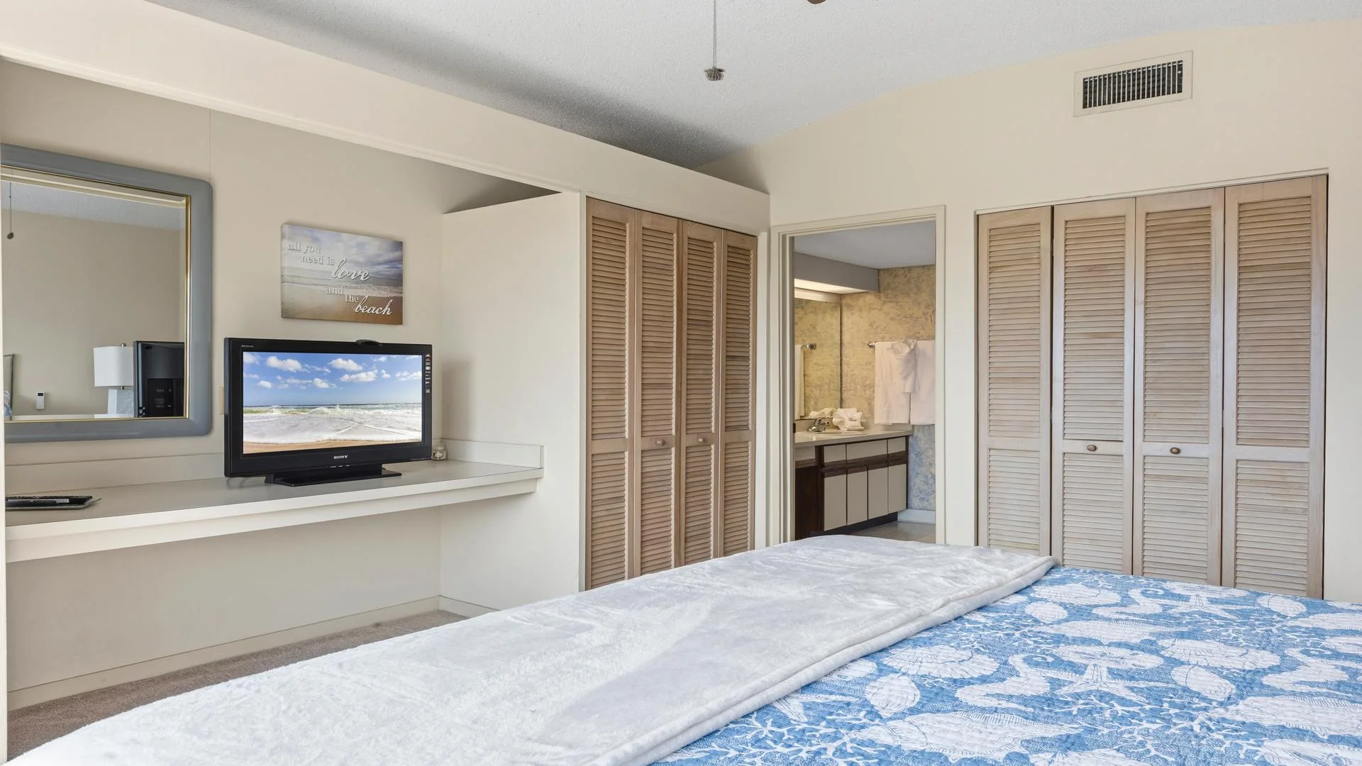 Bedroom view featuring a blue seashell-patterned bedspread, closet with louvered doors, and a wall-mounted TV.