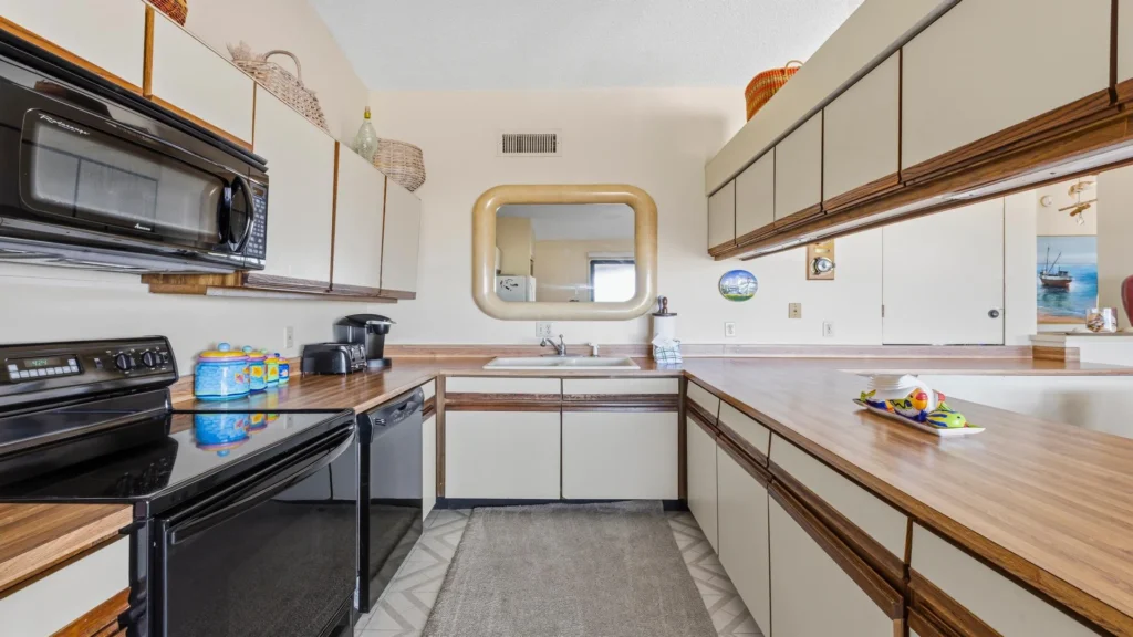 U-shaped kitchen with wood laminate countertops, black appliances, beige cabinets, and a large rounded-edge wall mirror.