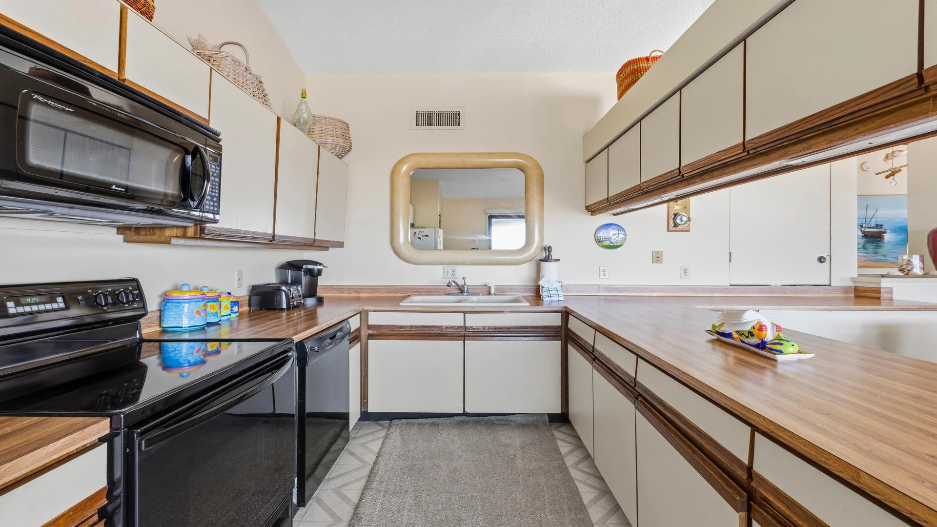 U-shaped kitchen with wood laminate countertops, black appliances, beige cabinets, and a large rounded-edge wall mirror.