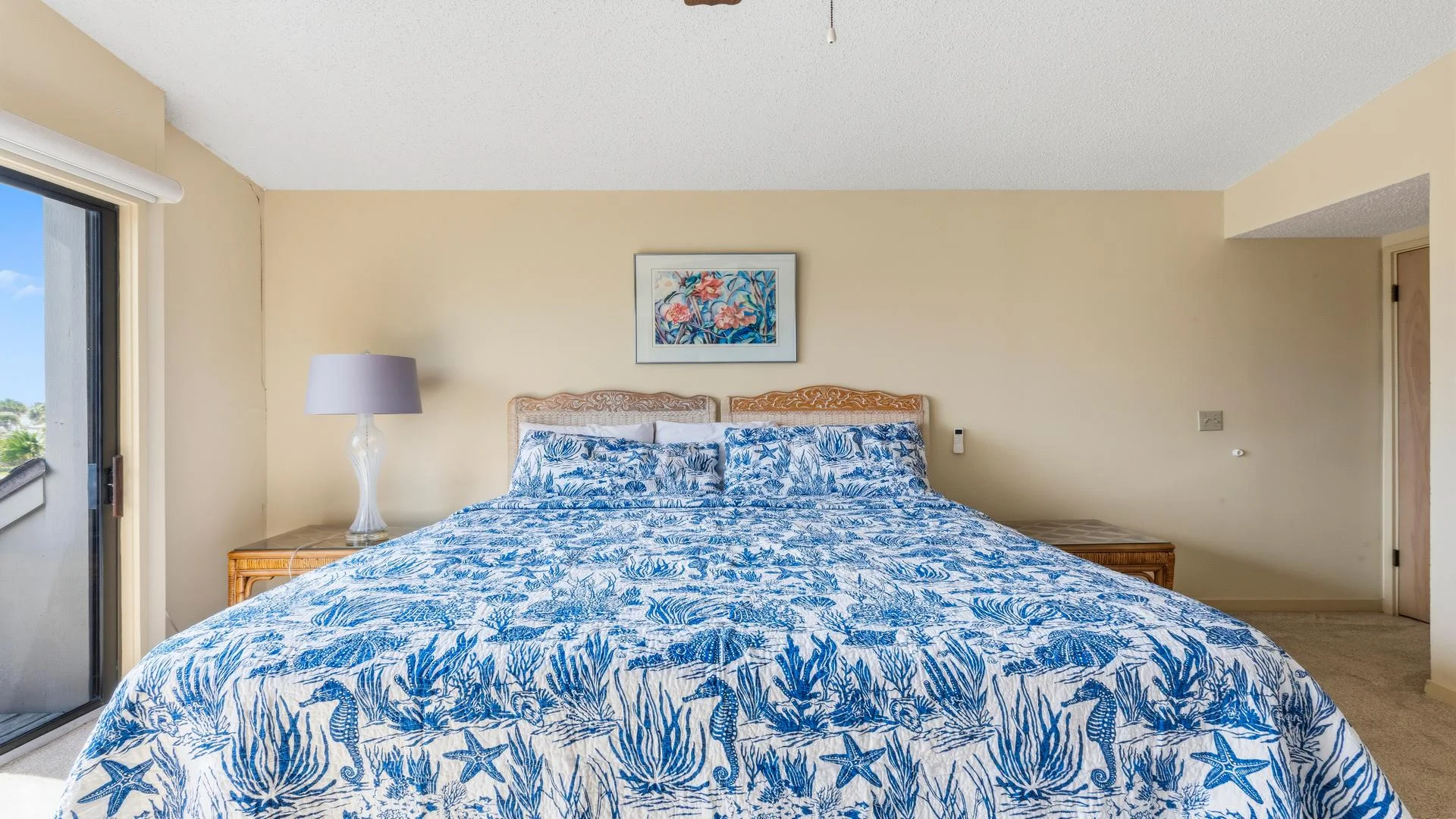 Two carved wood headboards rest against a beige wall above a bed dressed in blue and white sea life patterned bedding.
