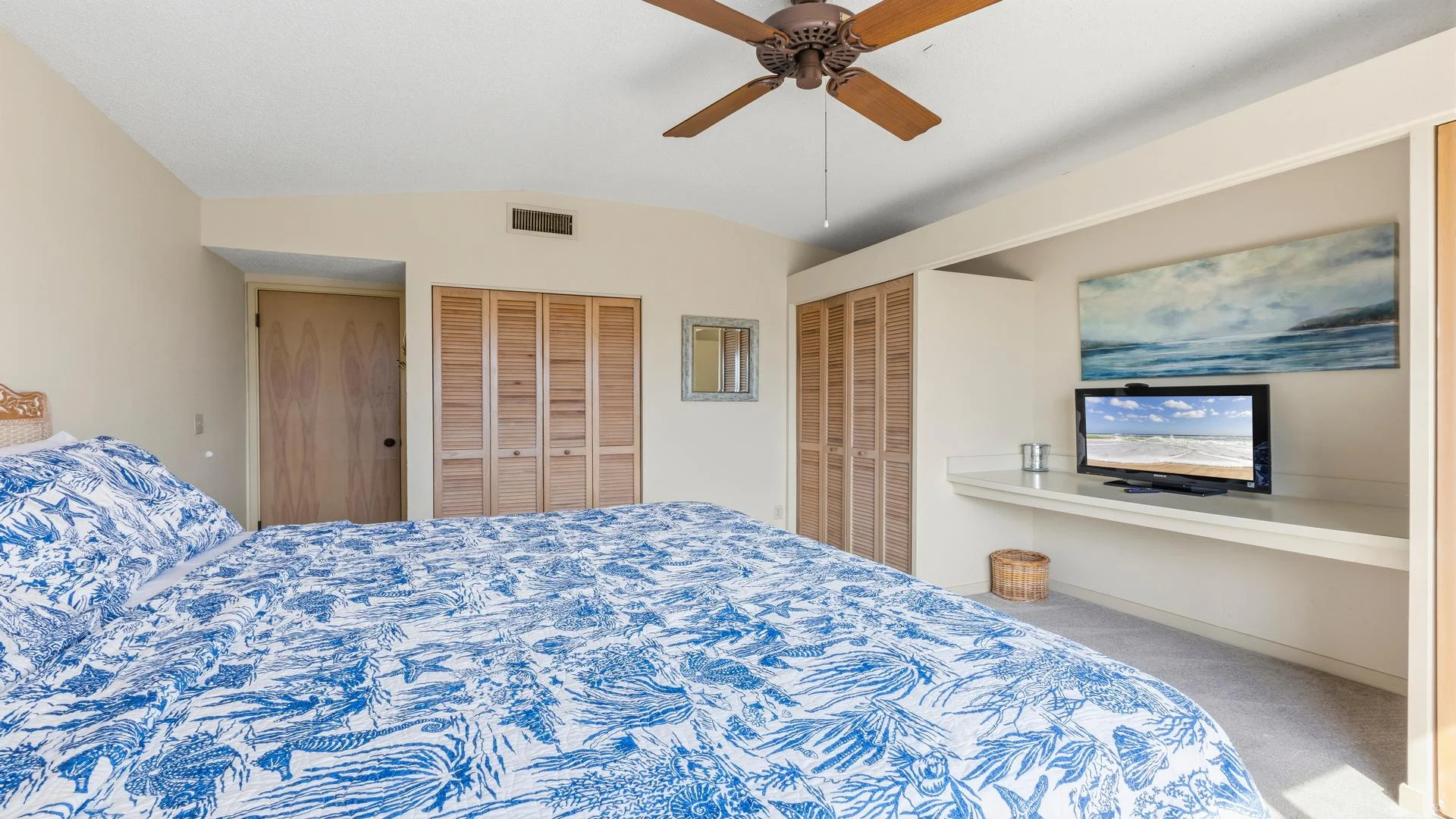 Built-in desk area under a seascape painting holds a flat-screen TV, with louvered closet doors nearby.