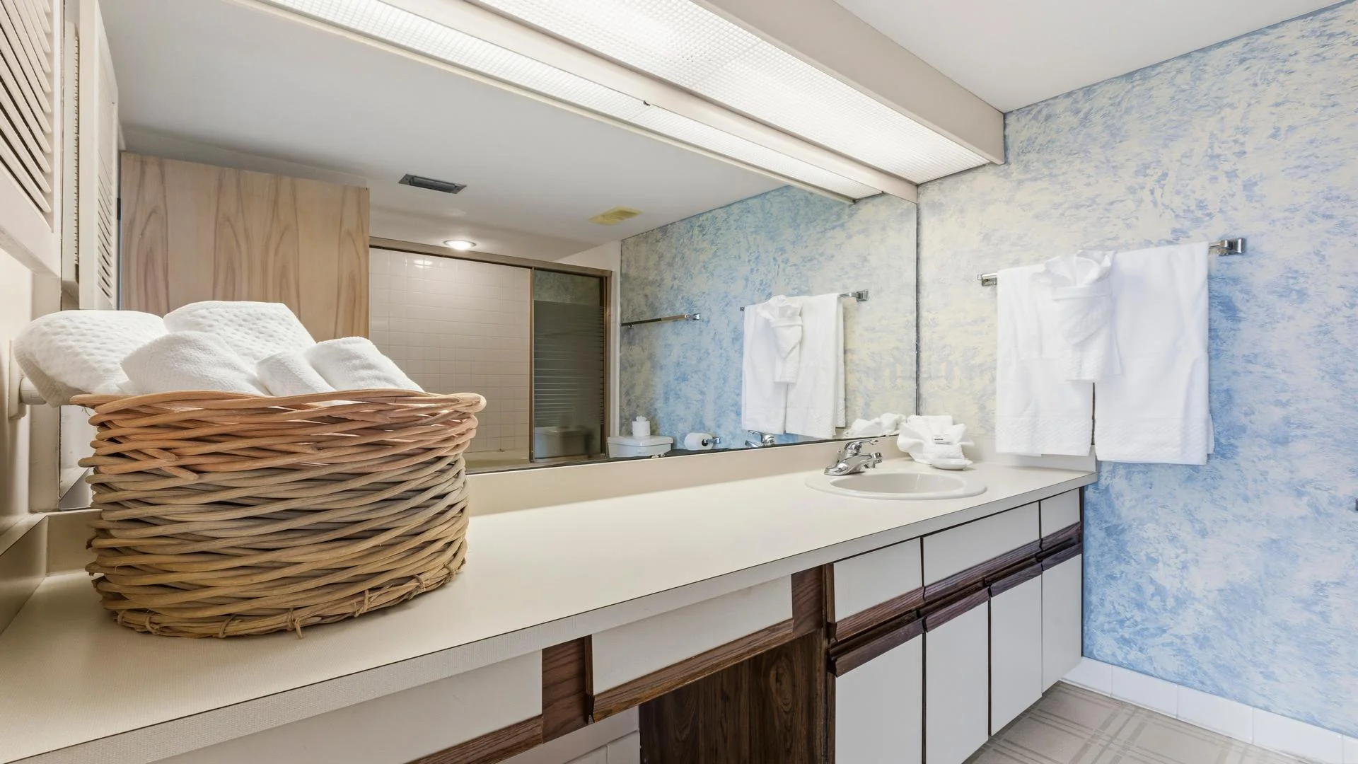 Bathroom countertop with built-in sink, wicker basket of rolled towels, and textured blue and white painted walls.
