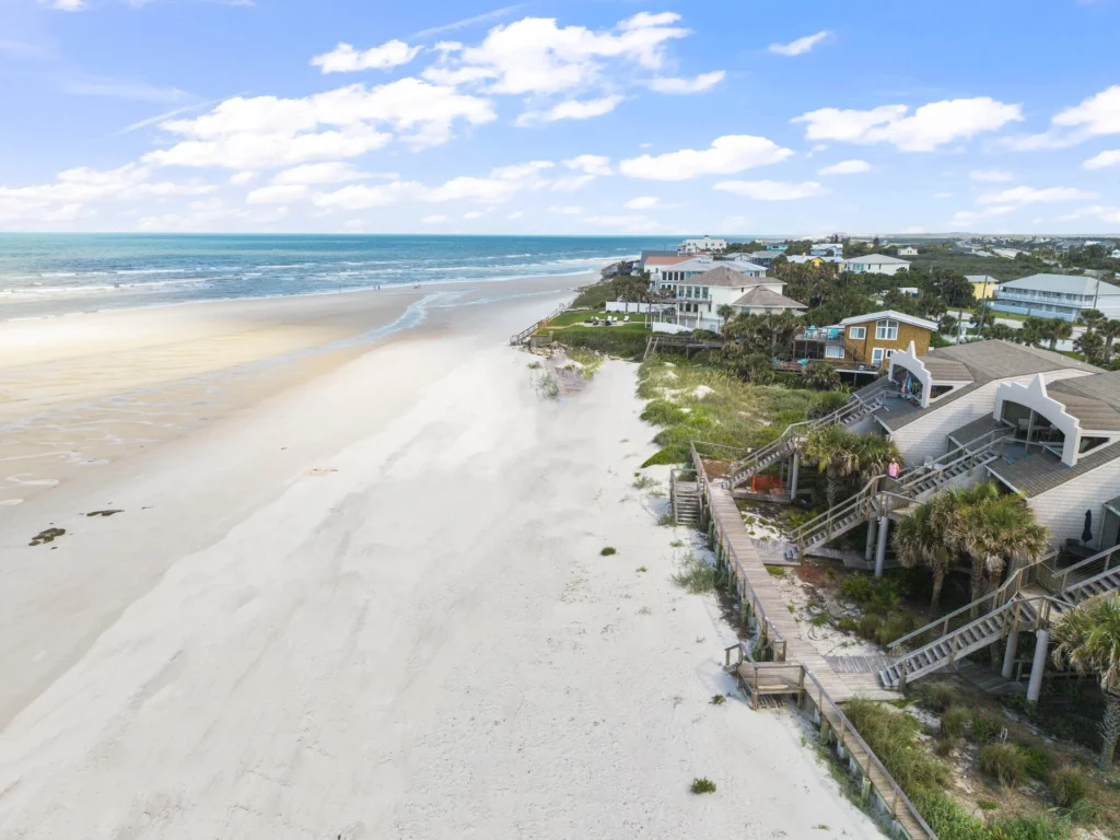 Aerial view of white sandy beach stretching alongside beachfront condos with wooden staircases and boardwalks.