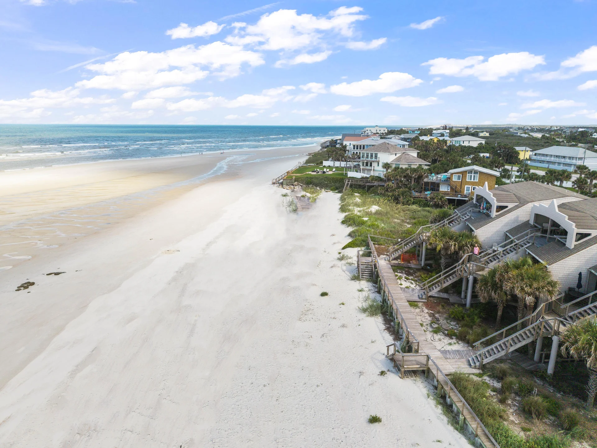 Aerial view of white sandy beach stretching alongside beachfront condos with wooden staircases and boardwalks.