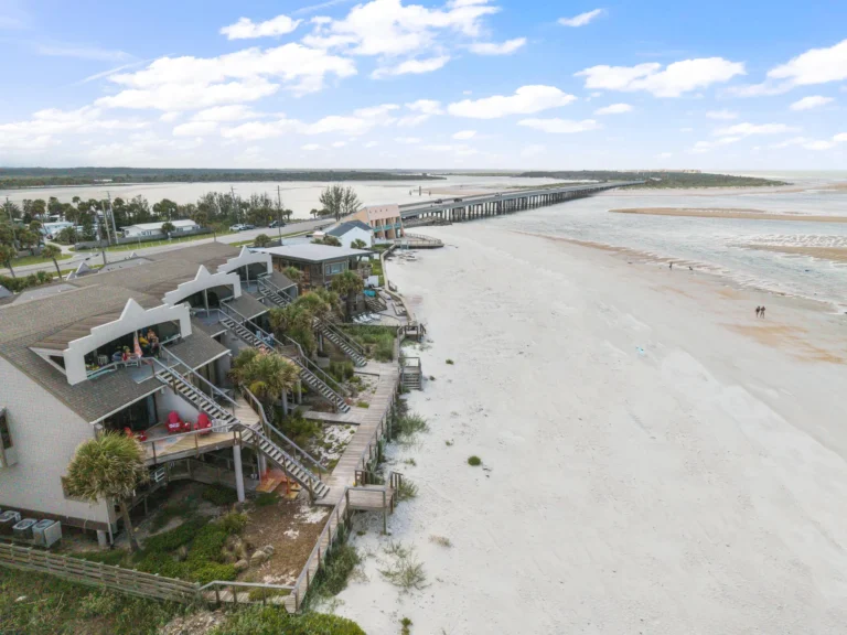 Aerial view of beachfront condos with wooden staircases descending to white sandy beach and ocean.