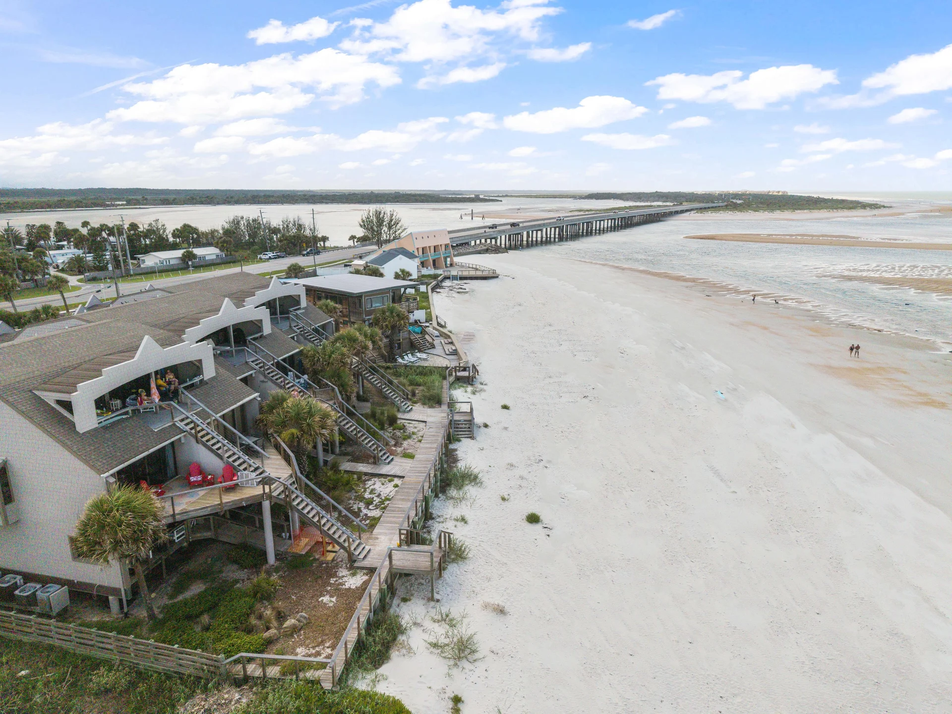 Aerial view of beachfront condos with wooden staircases descending to white sandy beach and ocean.