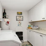Laundry room with white washer and dryer, granite countertop, white cabinetry, and decorative wall signs.