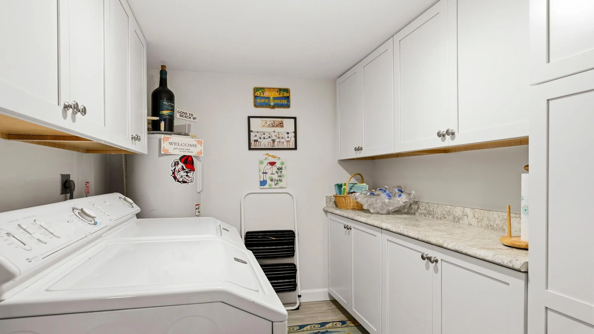 Laundry room with white washer and dryer, granite countertop, white cabinetry, and decorative wall signs.