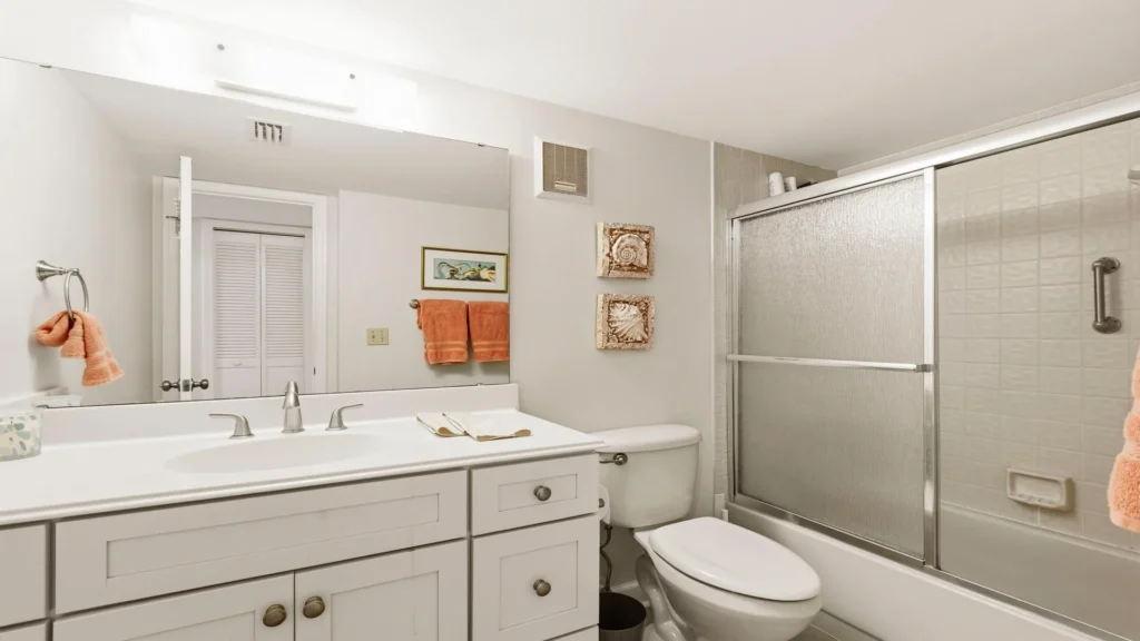Bathroom with white cabinetry, dual-sink vanity, textured glass shower doors, and coral-colored towels.