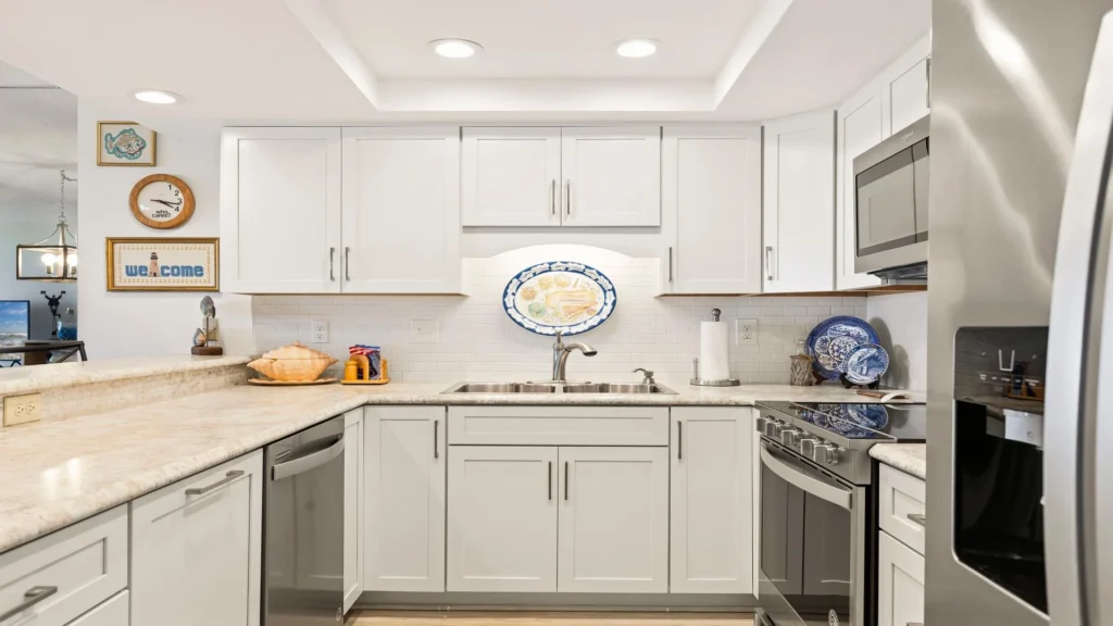 White cabinetry and marble countertops surround a stainless steel sink and modern appliances in the kitchen.