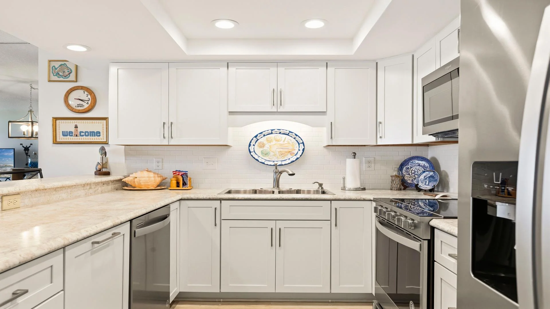 White cabinetry and marble countertops surround a stainless steel sink and modern appliances in the kitchen.