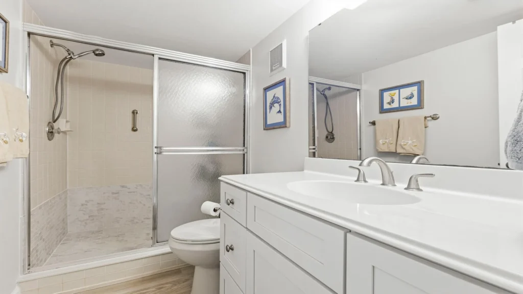 Bathroom features a walk-in shower with sliding frosted glass doors, tile surround, and a white vanity.