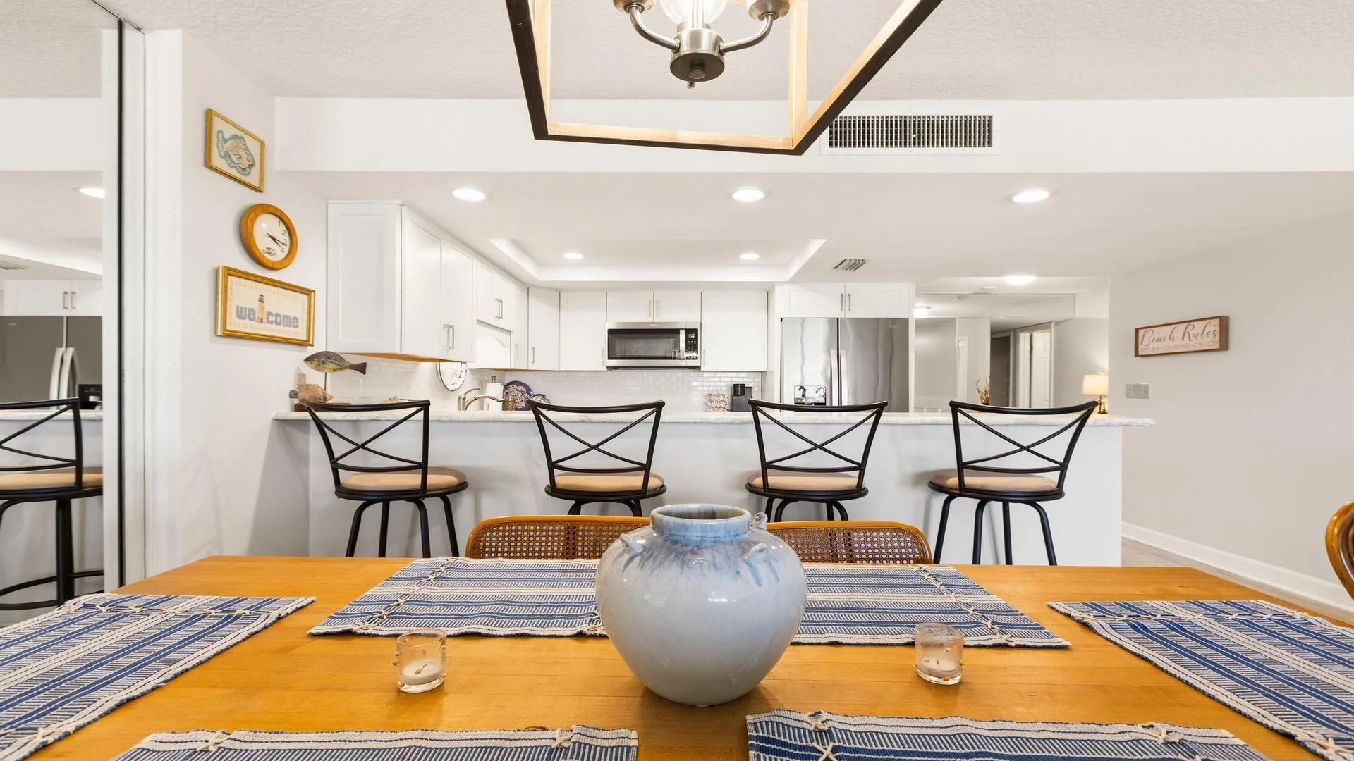 Dining table with woven chairs and a blue-and-white vase faces a breakfast bar with four cushioned stools.