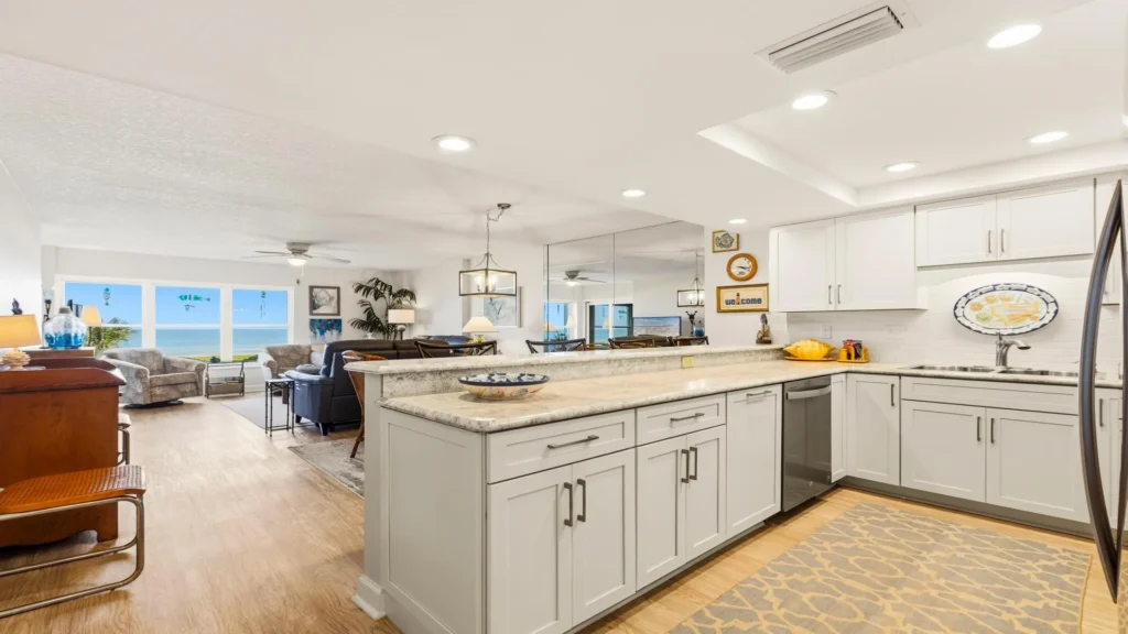 Open-concept kitchen with light gray cabinets, granite countertops, stainless steel appliances, and ocean views beyond the living area.