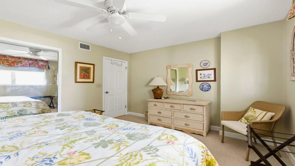 Wicker dresser topped with a ceramic lamp and scalloped-edge mirror, flanked by framed art and decorative plates.