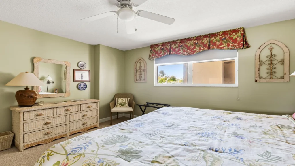 Natural light brightens the pale green walls, wicker dresser, and floral-patterned bedding in the bedroom.