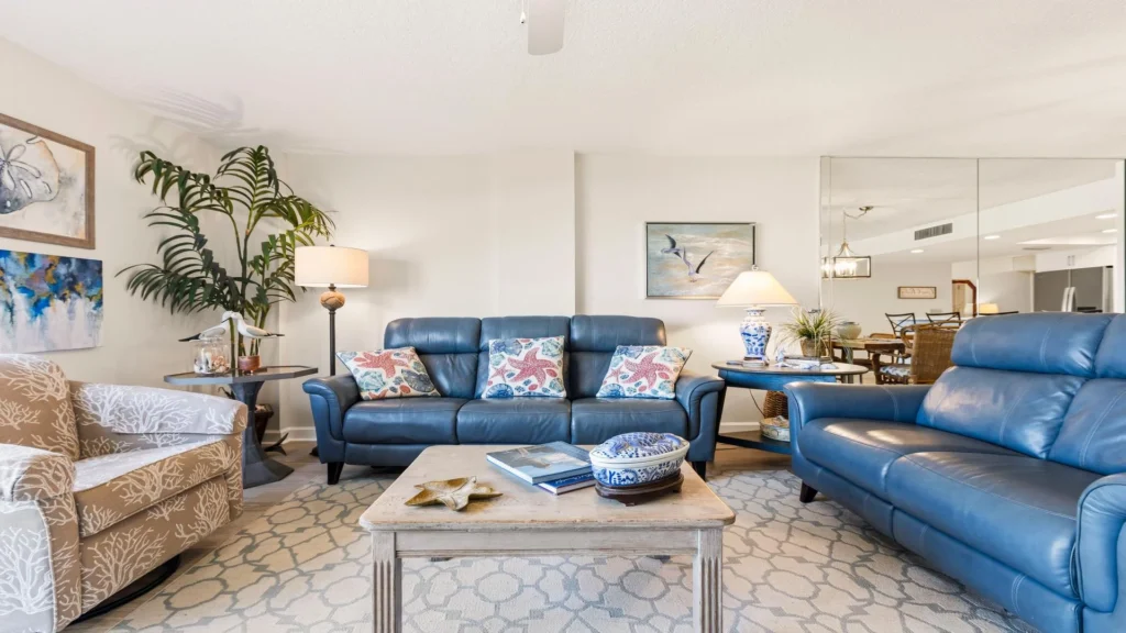 Living room with blue leather sofas, starfish-patterned pillows, beige coral-print armchair, and mirrored wall.