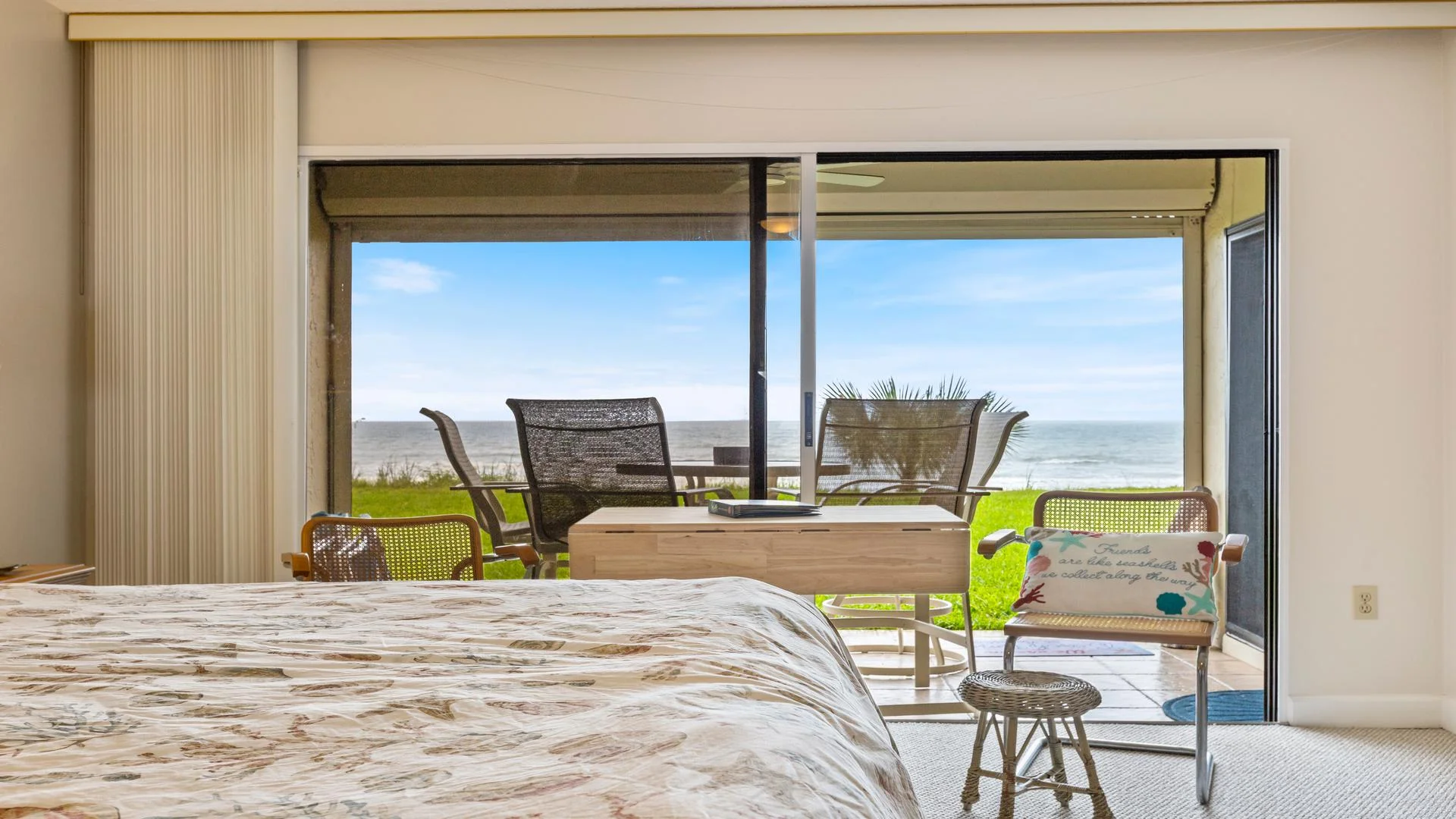 Sliding glass doors open to a covered patio with outdoor seating overlooking the ocean and grassy lawn.