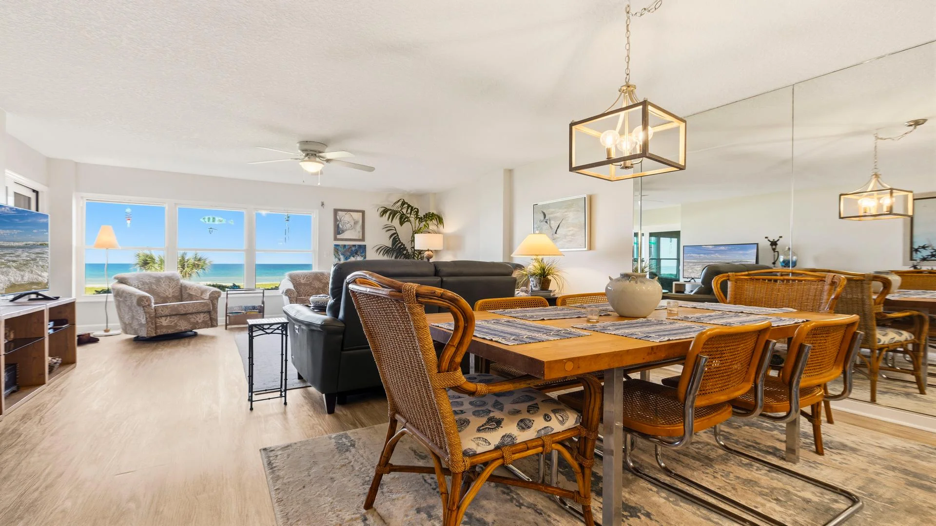 Wood dining table topped with a ceramic vase sits on a patterned rug beneath a geometric pendant light.