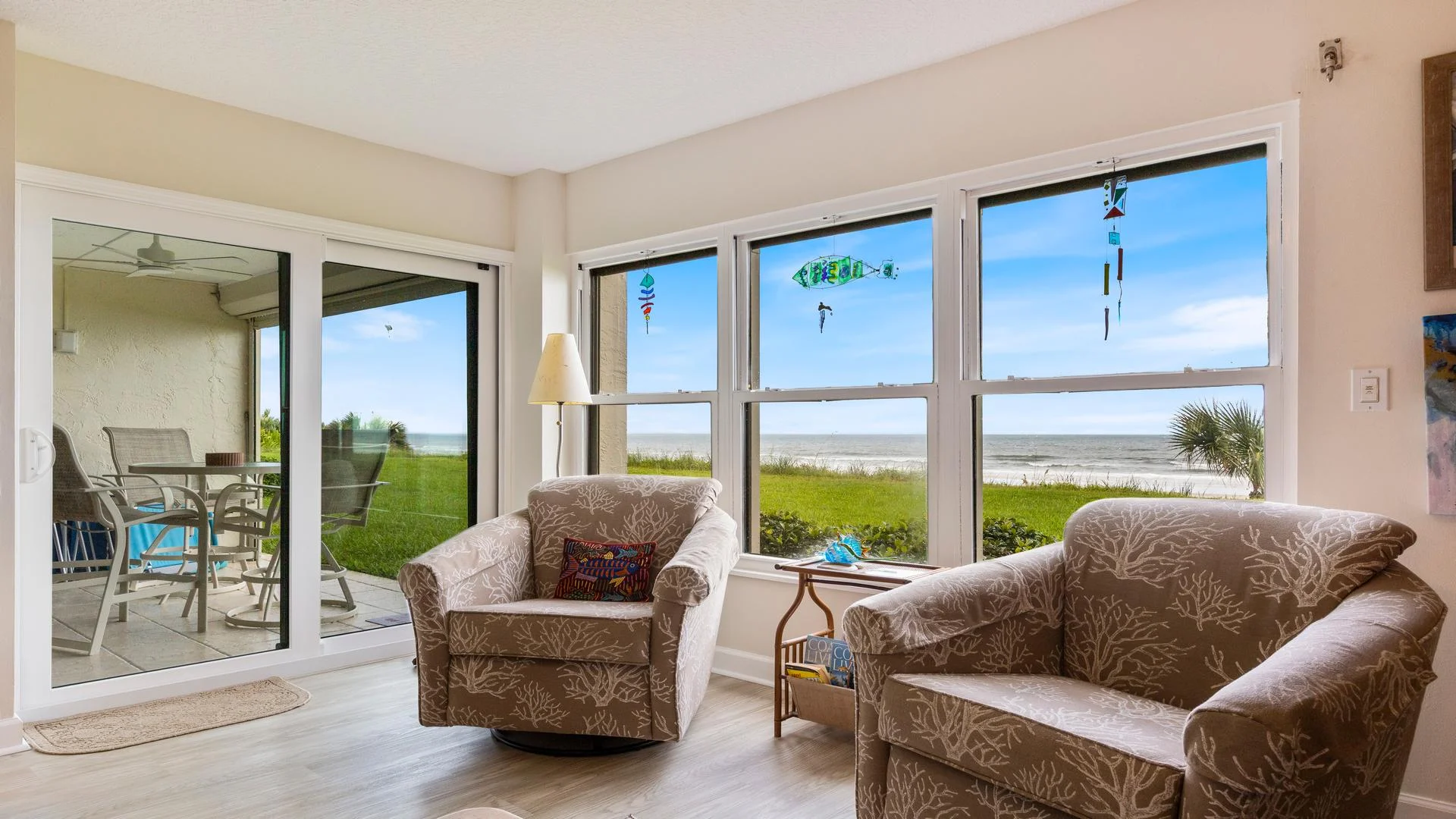 Living area features coral-patterned swivel chairs facing windows with ocean views and a sliding glass door to the patio.