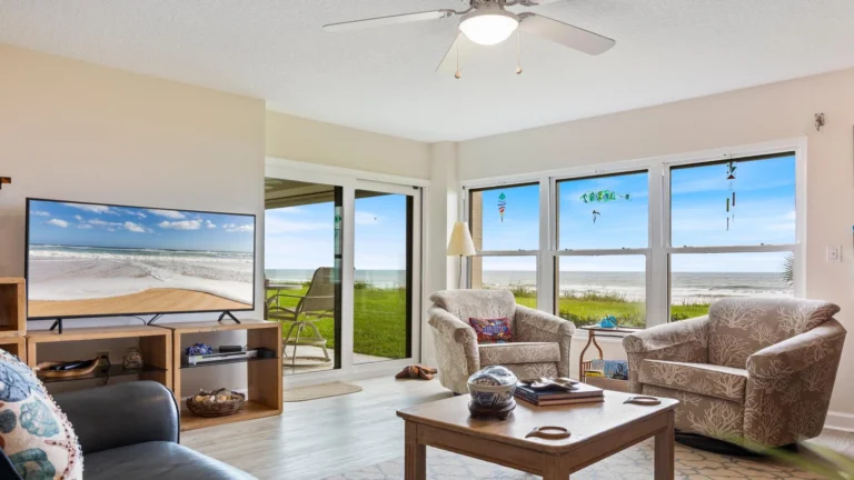 Living room with patterned armchairs, wooden coffee table, large windows, sliding glass door, and ocean views.