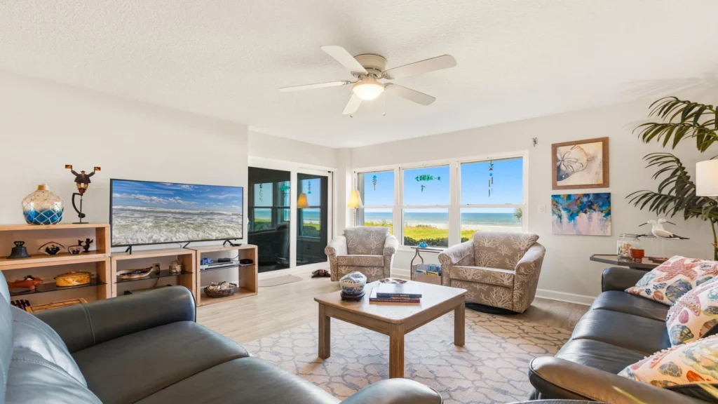 Living room with leather sofas, patterned armchairs, wood coffee table, and ocean views through large windows.