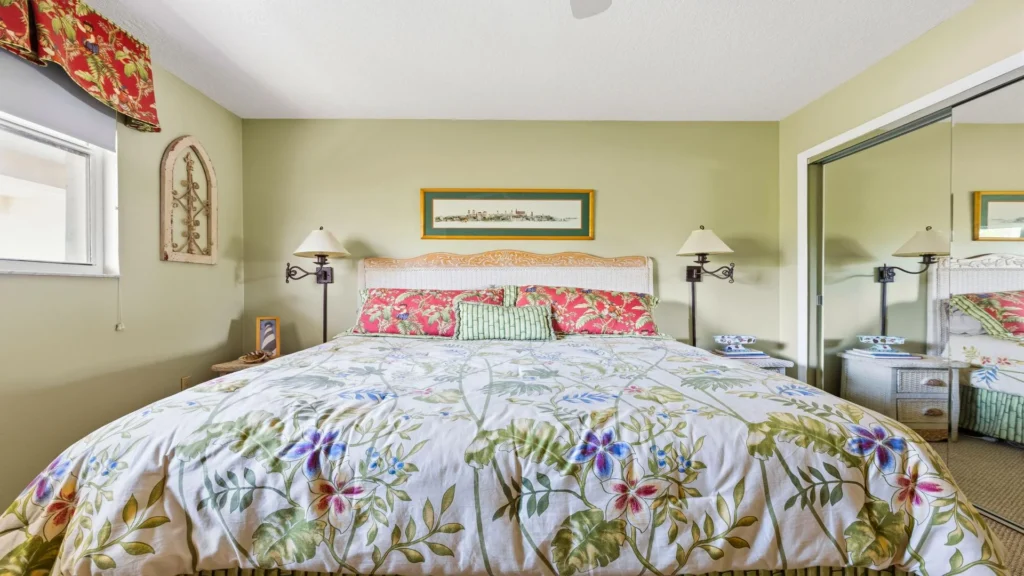 Wicker headboard frames the king bed topped with floral and leafy patterned bedding in the green-walled bedroom.