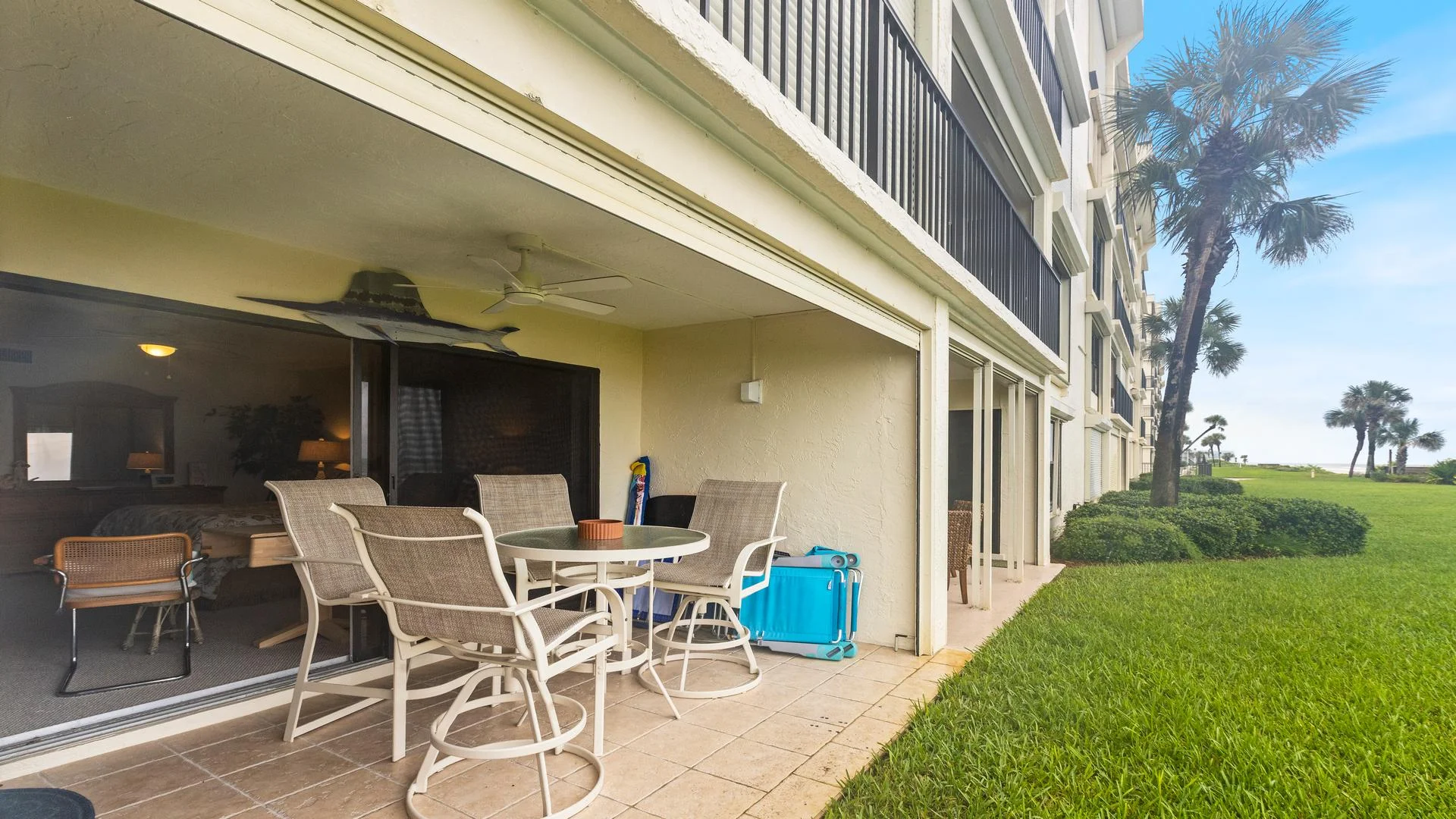 Outdoor patio with beige tile flooring, swivel chairs around a glass-top table, and sliding glass doors opening to the bedroom.