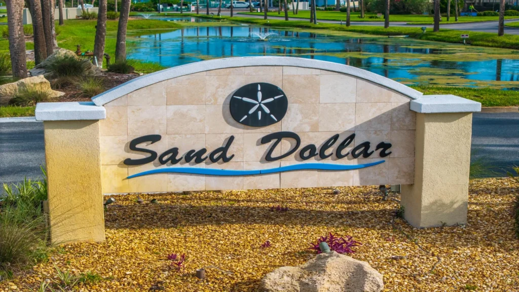 Entry sign for the Sand Dollar community features stone tiles, black script lettering, and a black sand dollar emblem.