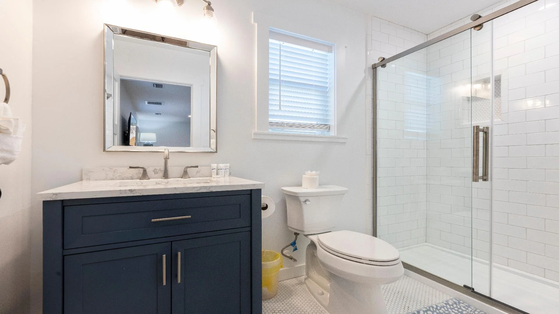 Bathroom features a navy blue vanity with marble countertop, glass-enclosed shower, and hex tile floor.