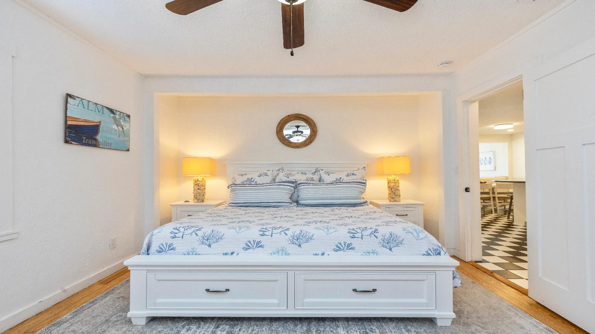 King bed with blue sea life bedding, flanked by shell-textured lamps on white nightstands.