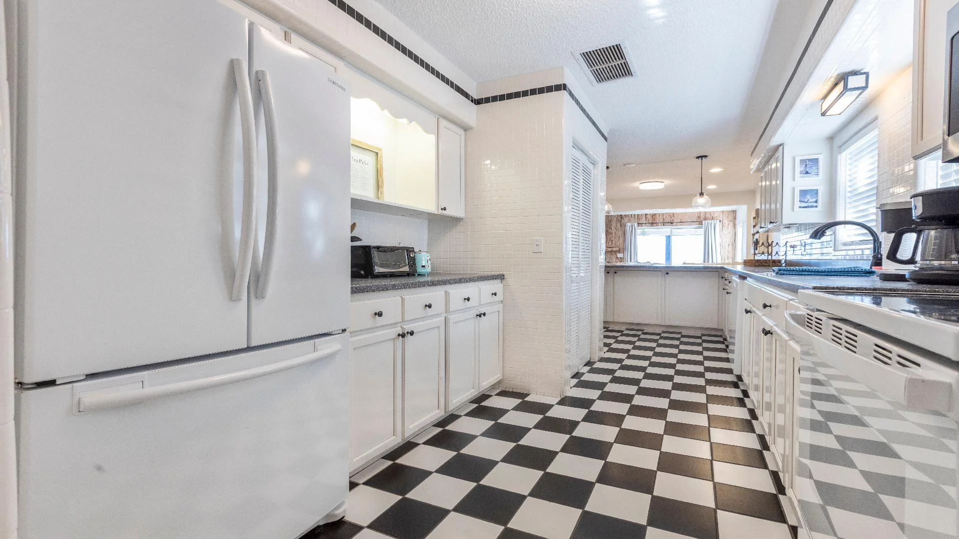 Galley kitchen with black-and-white checkered tile flooring, white cabinetry, and stainless steel appliances.