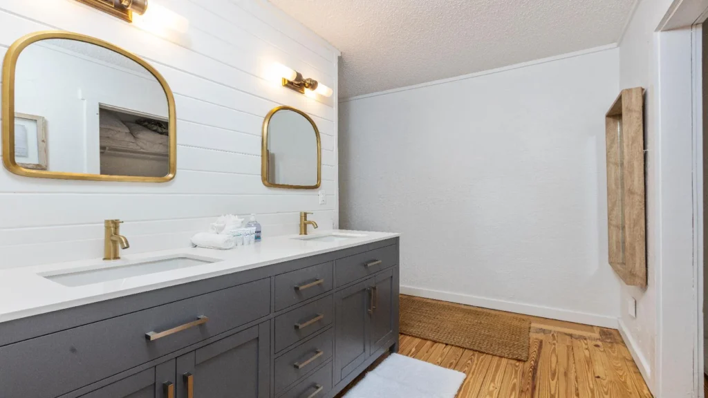 Double-sink vanity with matte gold fixtures and arched mirrors against white shiplap walls in the bathroom.