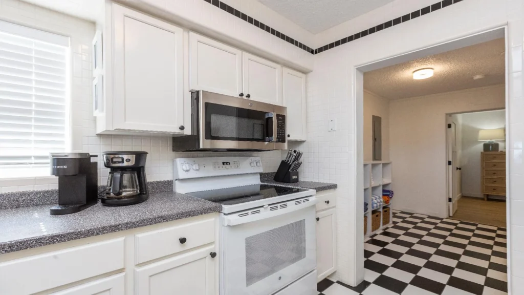 Black and white checkerboard tile floor leads from the kitchen with white cabinetry and stainless steel microwave.