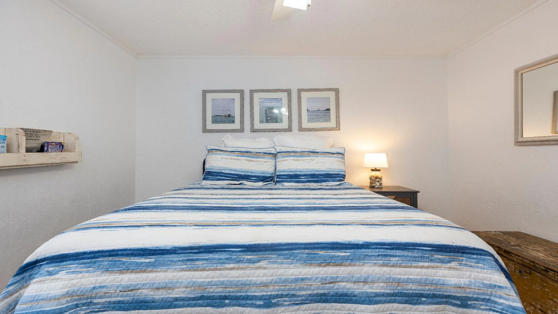 King bed with blue and beige striped bedding, nautical-themed prints above, and a rustic nightstand lamp.