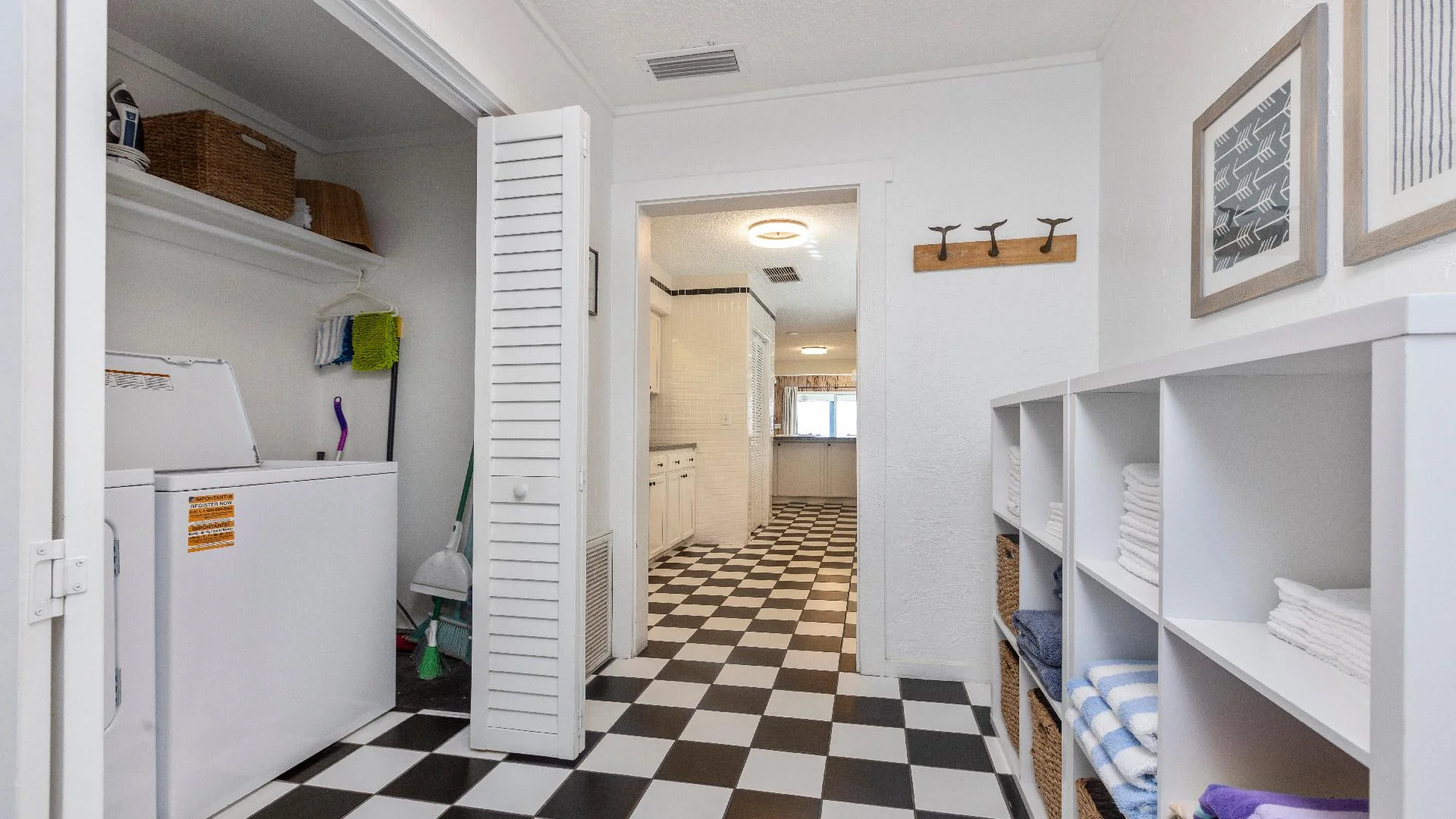 Laundry area with top-loading washer, cleaning supplies, and white cubbies holding folded towels and baskets.
