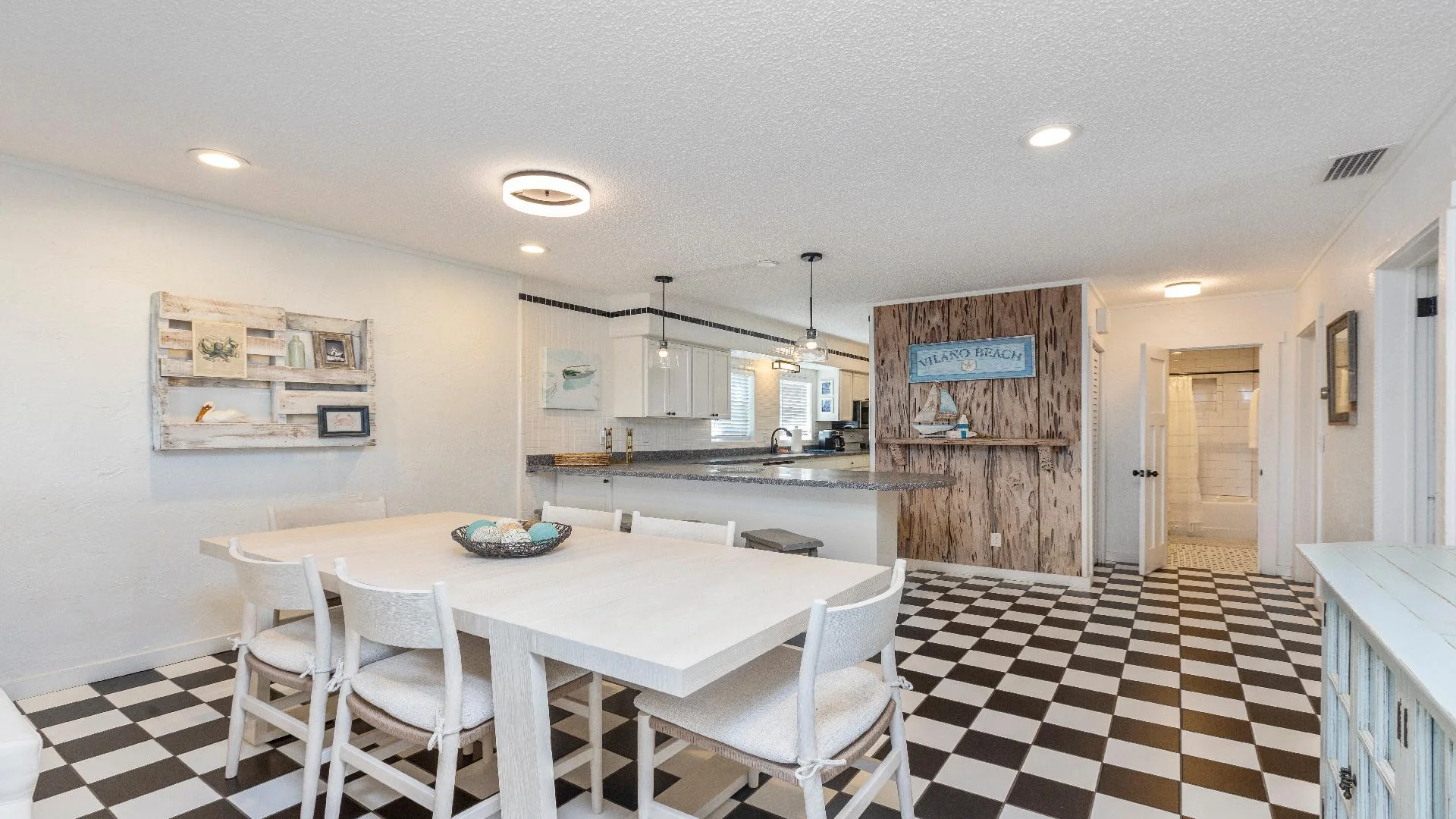 Black-and-white checkerboard floor extends beneath a white dining table and chairs, with a rustic wood accent wall.