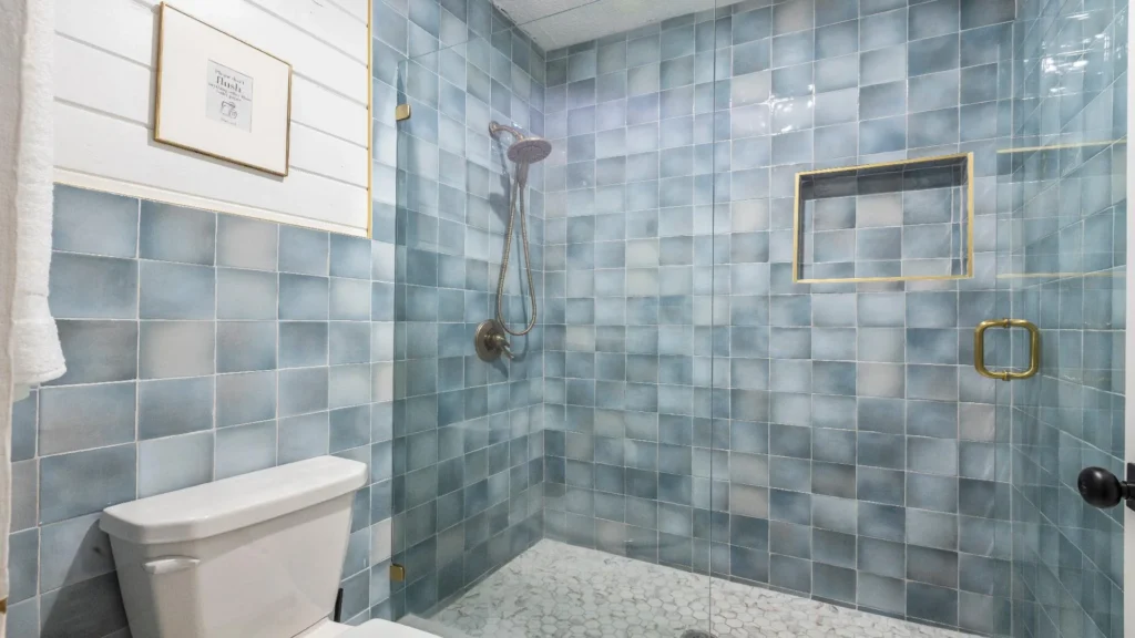 Shower area with glass enclosure, blue square tiles, brass trim niche, and hexagonal marble floor tiles.