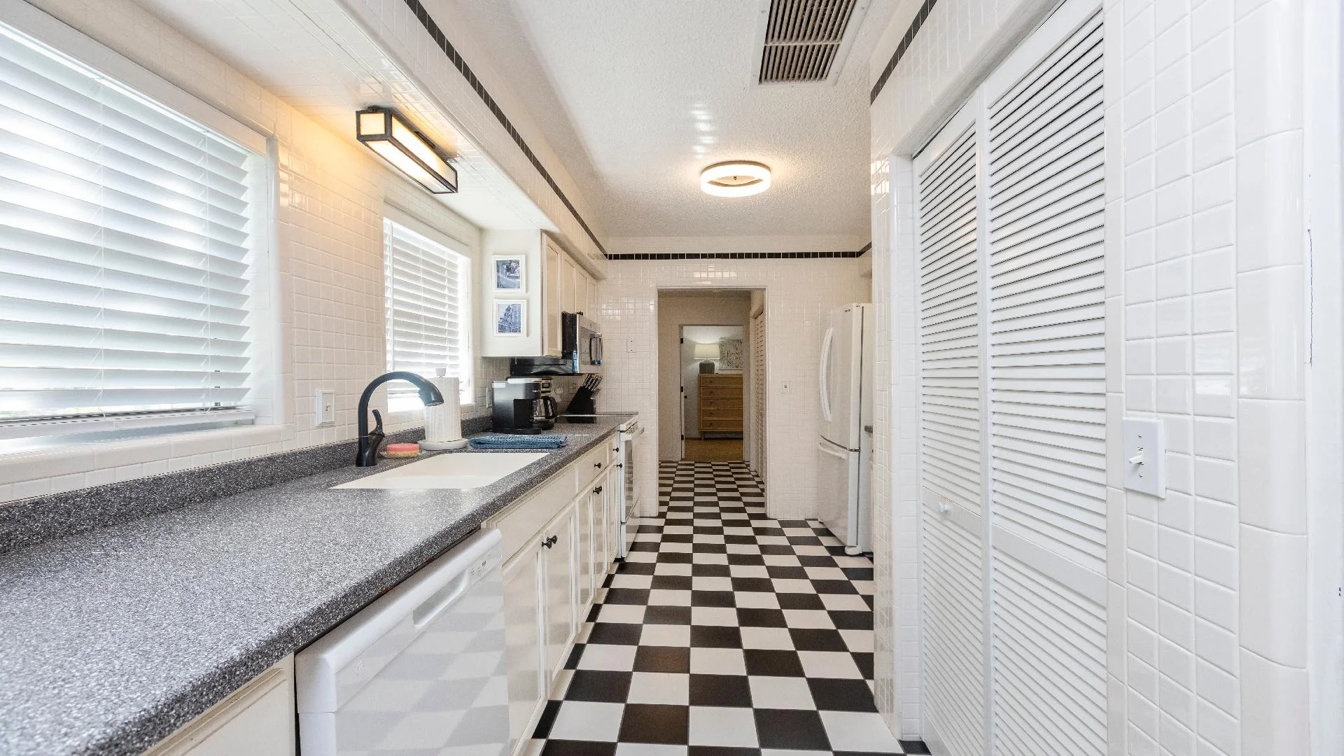 Long granite-look countertop with undermount sink sits below two wide windows with white blinds.